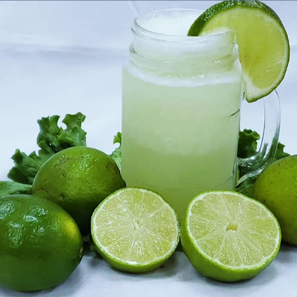 A glass of refreshing limeade garnished with a lime slice, surrounded by whole and halved limes.