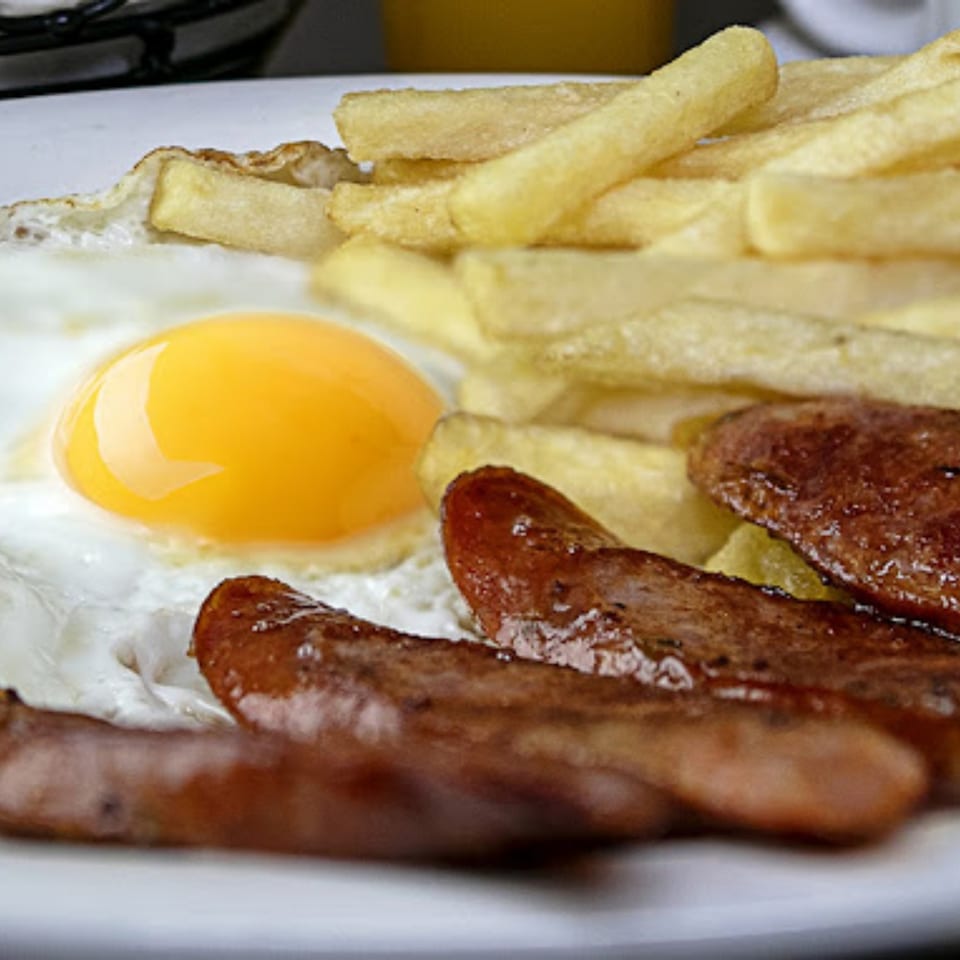 A Cuban breakfast plate with a fried egg, crispy french fries, and three browned sausages.