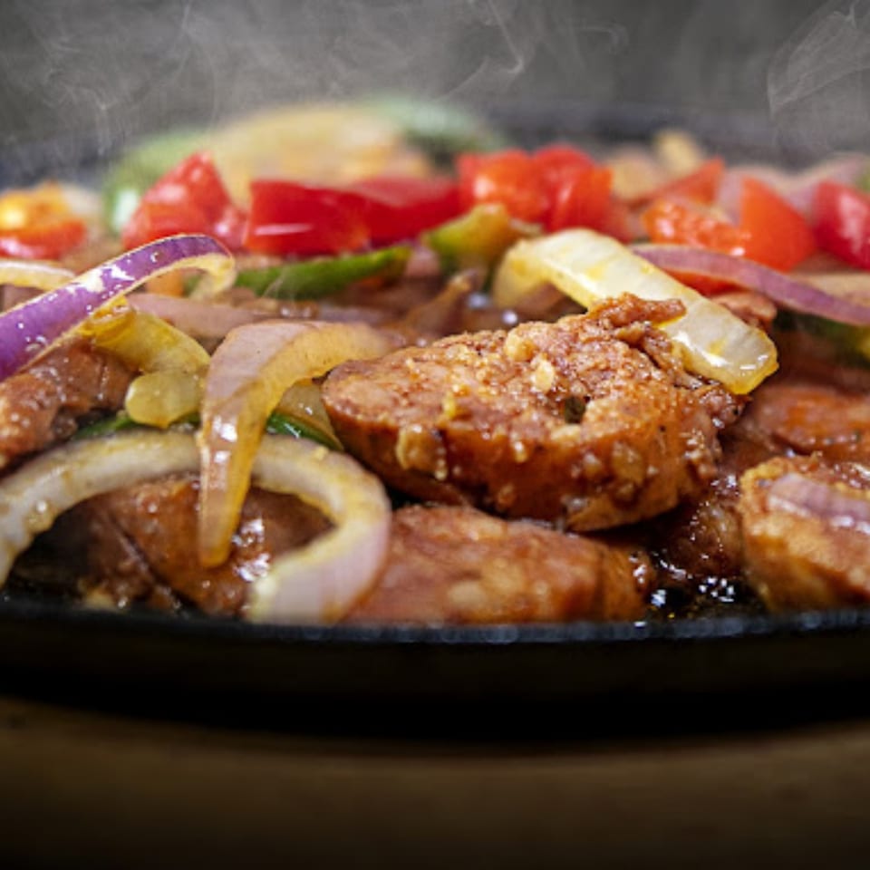 Sizzling Cuban chorizo with red and green peppers, and onions, steaming on a hot plate.