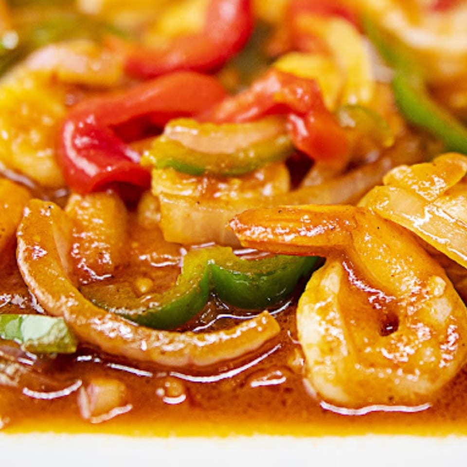 Close-up of Cuban shrimp dish with red and green bell peppers, onions, and a rich sauce.