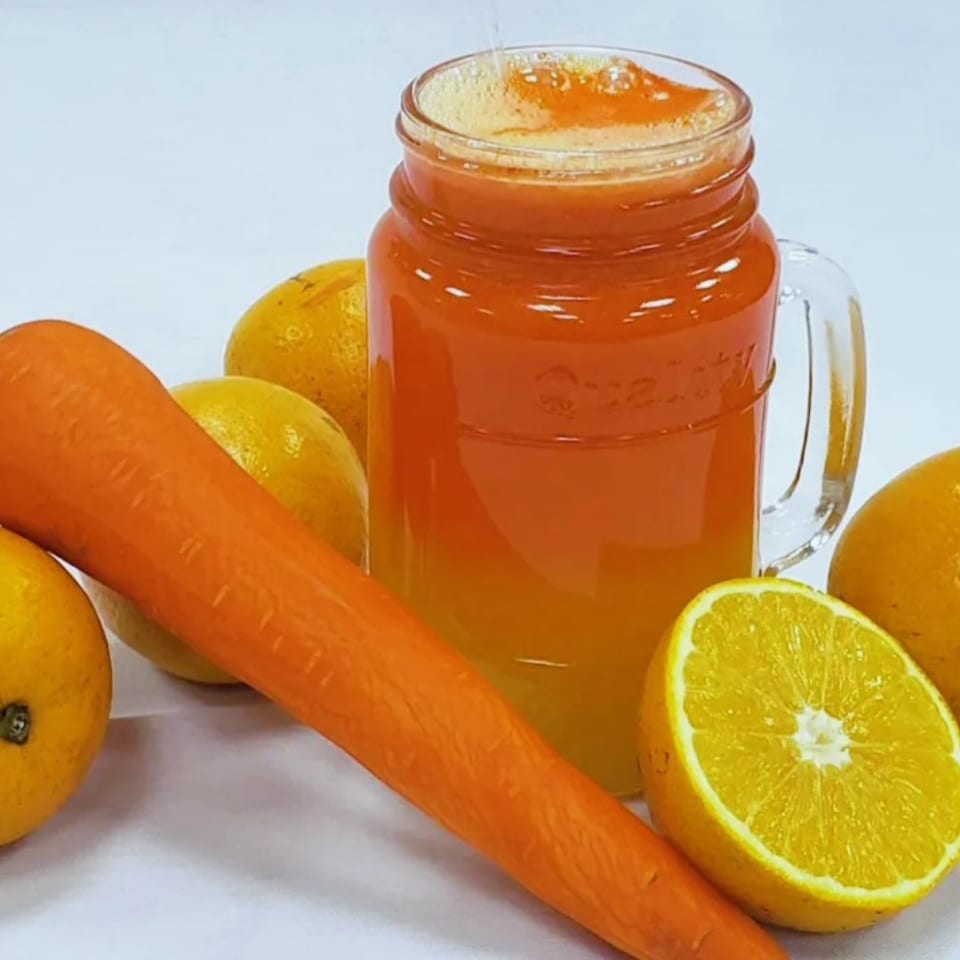 Freshly poured orange and carrot juice in a mason jar, surrounded by whole and halved oranges and a carrot.
